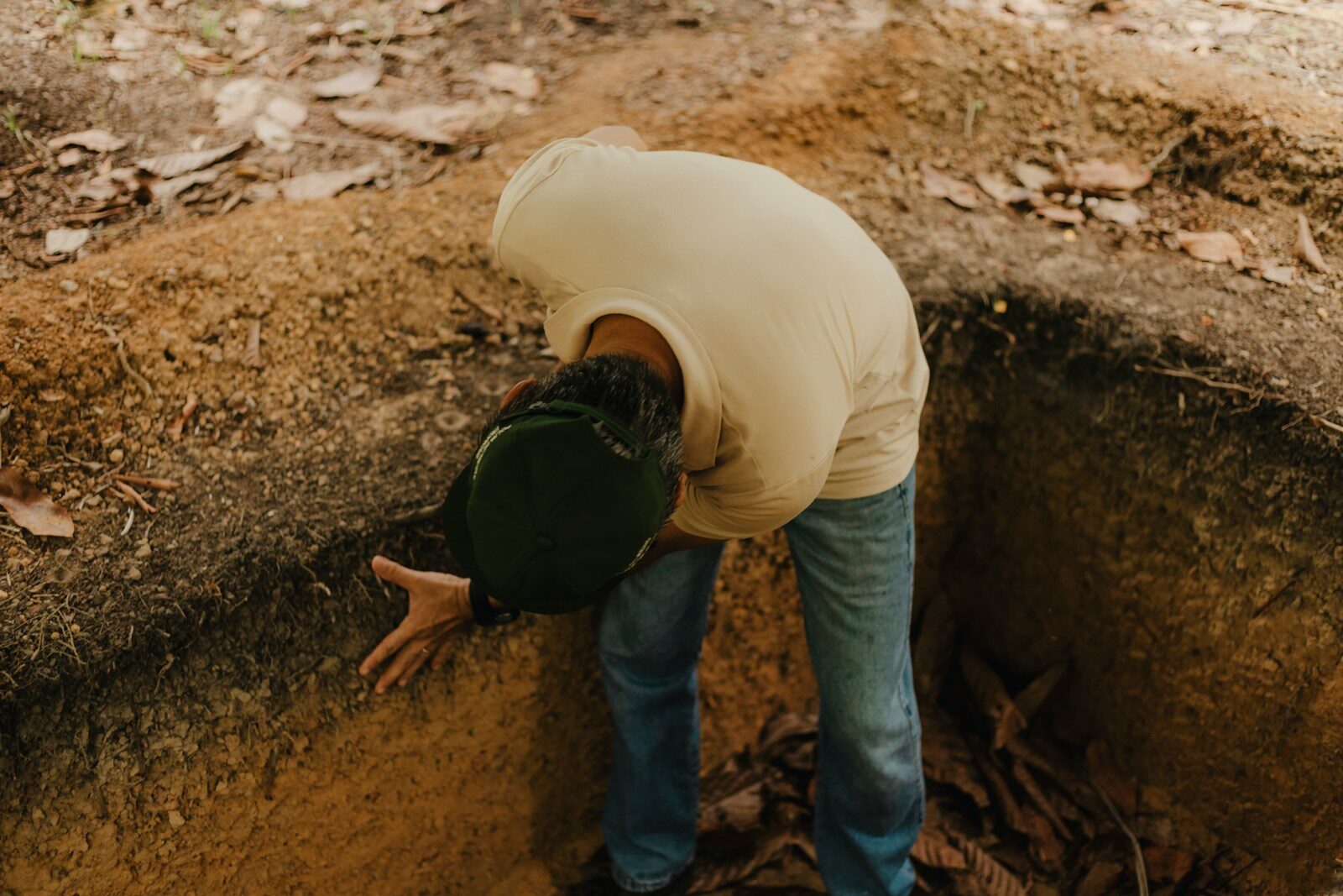 A man in a white shirt is digging a hole in the ground